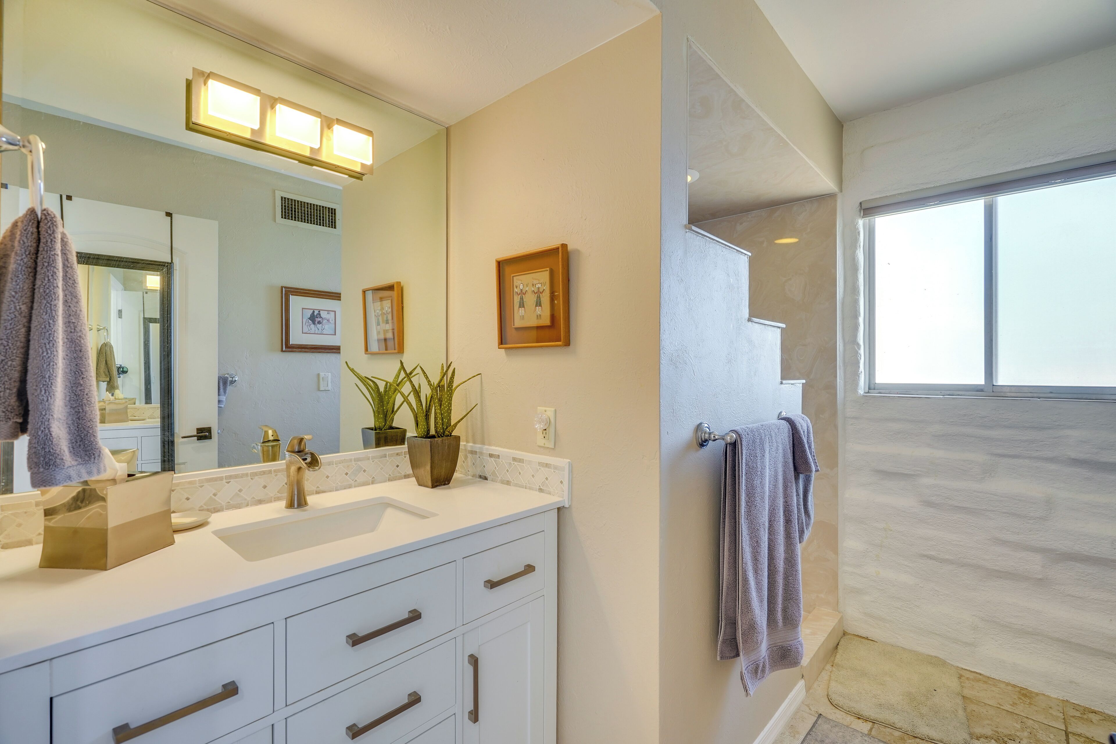 Une salle de bain moderne avec un grand miroir, un meuble-lavabo blanc et une plante en pot.