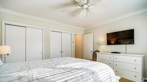 A bedroom with a large bed, a ceiling fan, a dresser, and a TV on the wall. - Steps to Sand & Surf! Couples Haven in Brigantine (Brigantine)
