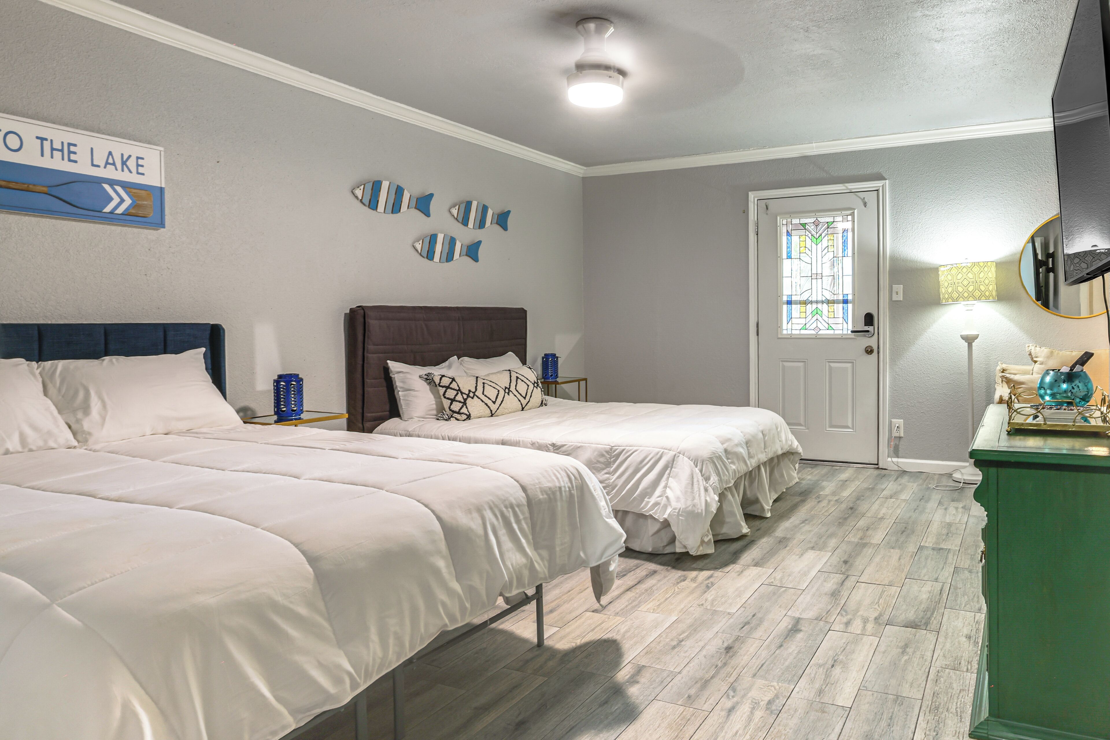 A bedroom with two beds, a wooden floor, a door with a stained glass window, and a wall with fish decorations.