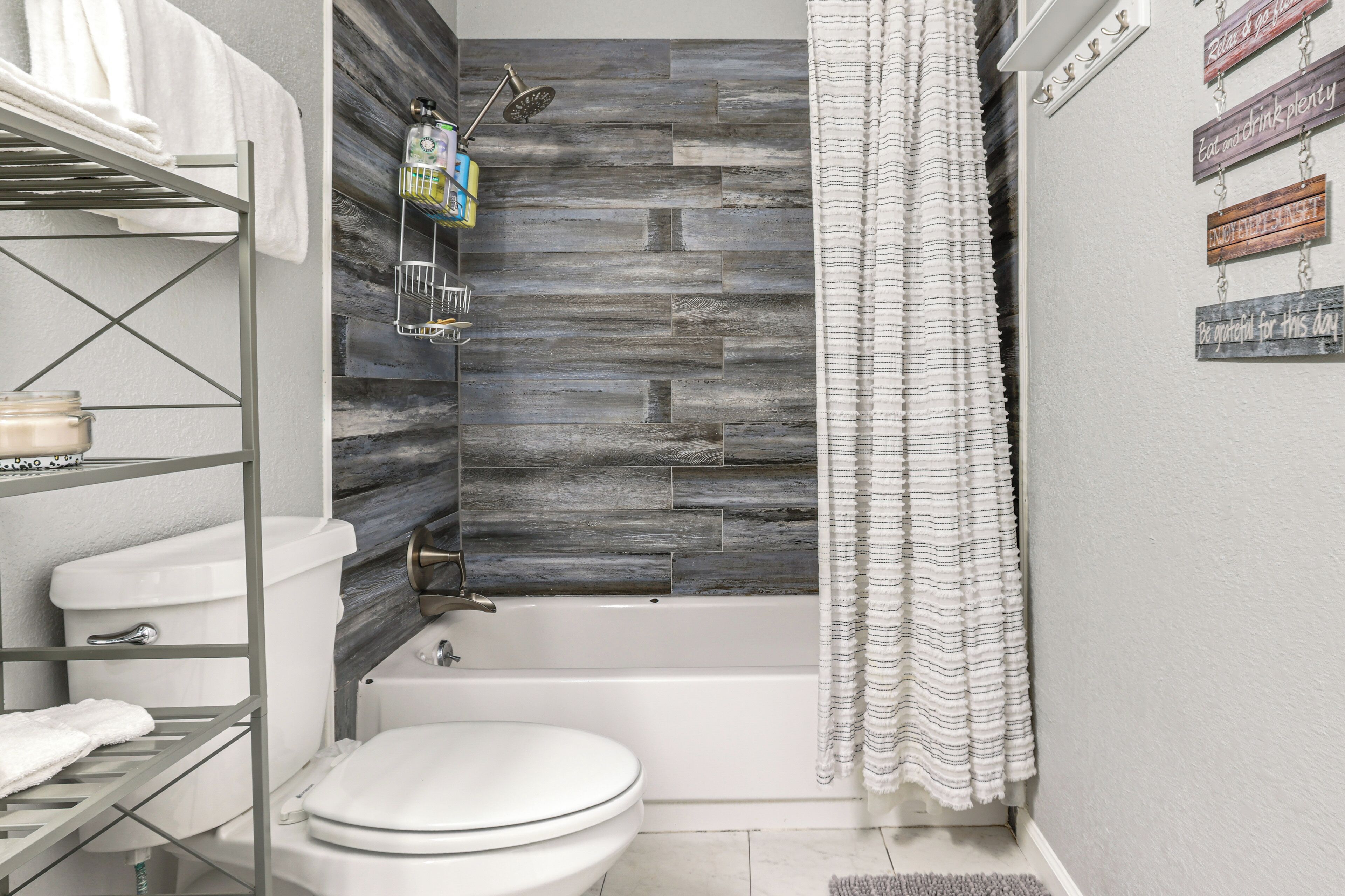 A bathroom with a modern design, featuring a white toilet, a bathtub, and a shower area with a rain showerhead. There are shelves with towels and toiletries.
