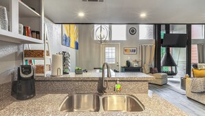 A modern kitchen with granite countertops, stainless steel sink, and a built-in oven. There is a dining area with a sofa and a coffee table. - Golf, Boat, Swim! Point Venture Retreat w/ Deck (Leander)