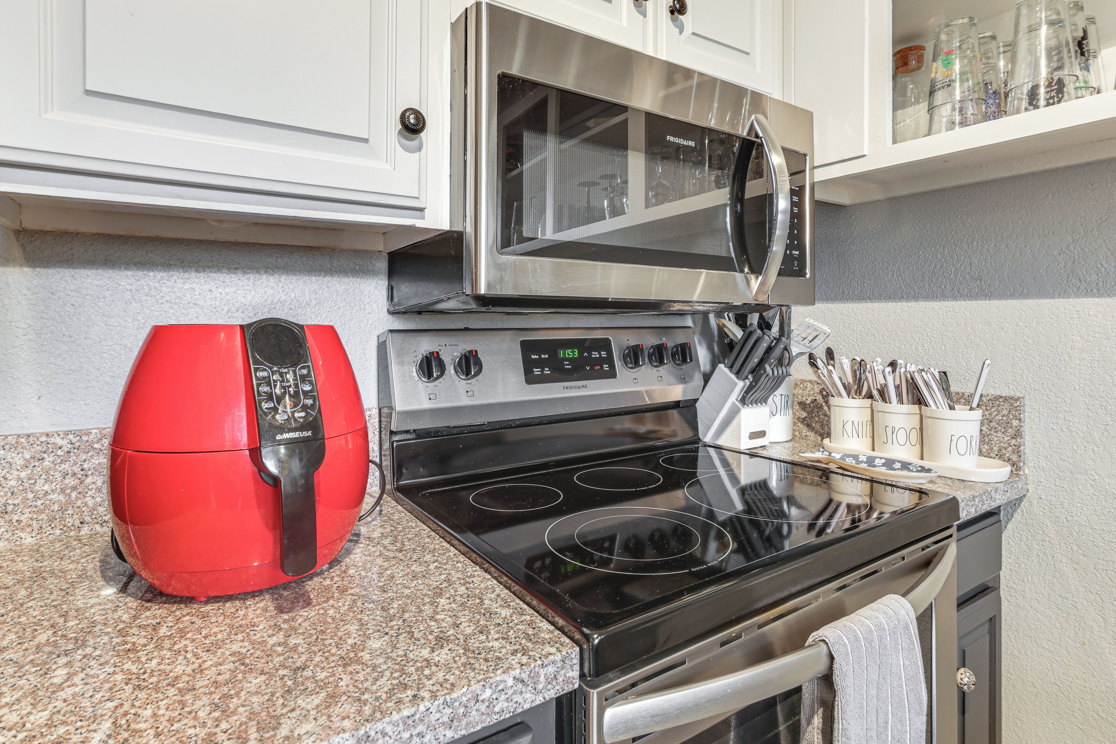 A kitchen with a stainless steel microwave, a red electric kettle, and a granite countertop.