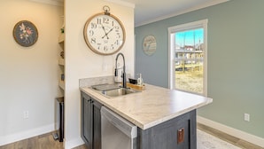 A kitchen with a marble countertop, a dishwasher, a sink, and two wall clocks. - Walk to Marina: Waterfront South Holston Lake Home (Bristol)