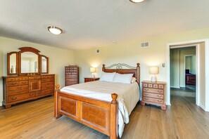 Quarto com cama de madeira, duas mesas de cabeceira, cômoda e um espelho grande.
