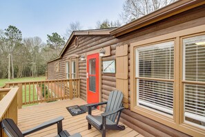 A log cabin with a deck, a red door, and a black chair. - Lakeside Retreat w/ Yard: Quiet Mississippi Cabin (Perkinston)