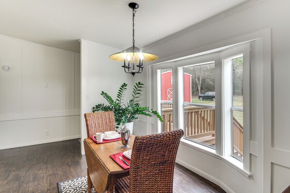 A dining area with a wooden table, wicker chairs, a hanging light fixture, and a view of a deck outside.