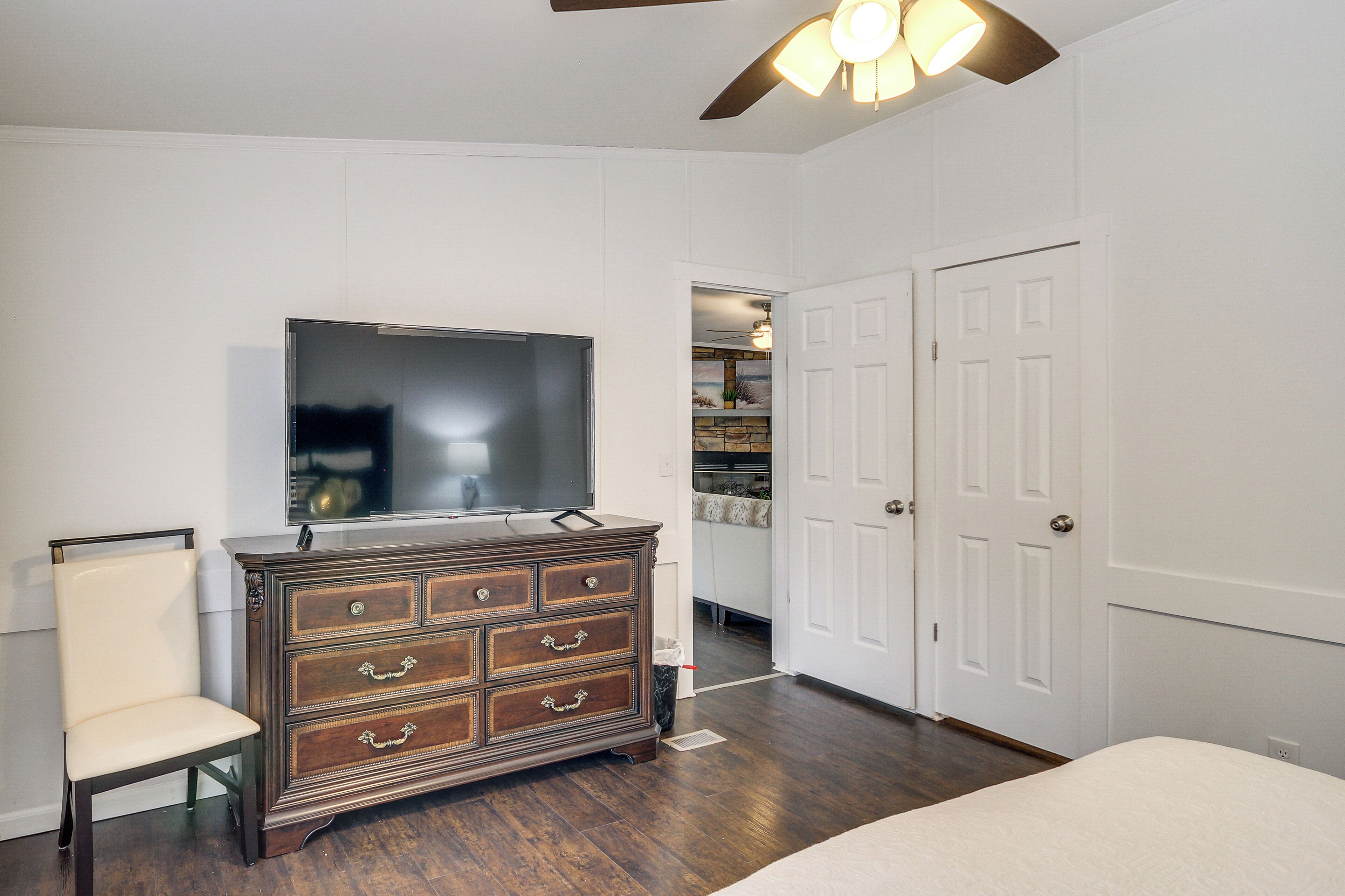 A bedroom with a wooden dresser, a television, a chair, and a closet with two doors.