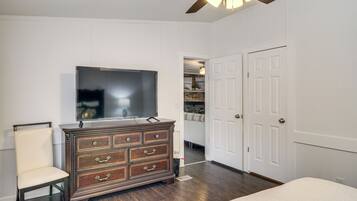 A bedroom with a wooden dresser, a television, a chair, and a closet with two doors.