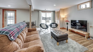 A modern living room with a sofa, ottoman, and chairs, a TV, and a view of the outdoors. - Explore the Northeast Kingdom! Home w/ Deck (Norton)