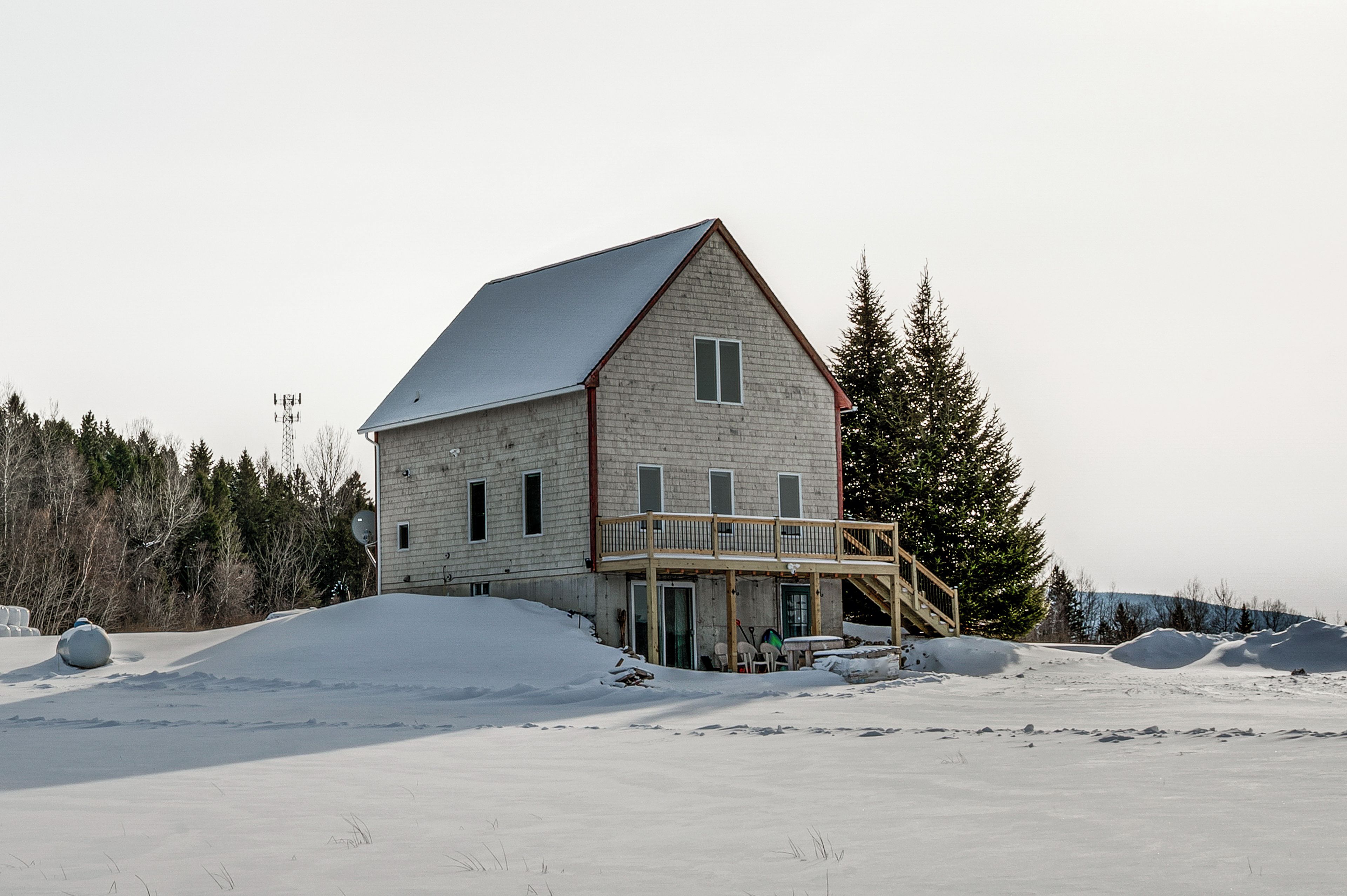 A two-story house with a balcony, surrounded by snow and trees.