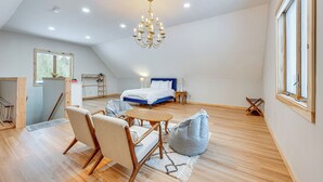 A spacious loft bedroom with a large bed, a chandelier, and a view of the outdoors. - Explore the Northeast Kingdom! Home w/ Deck (Norton)