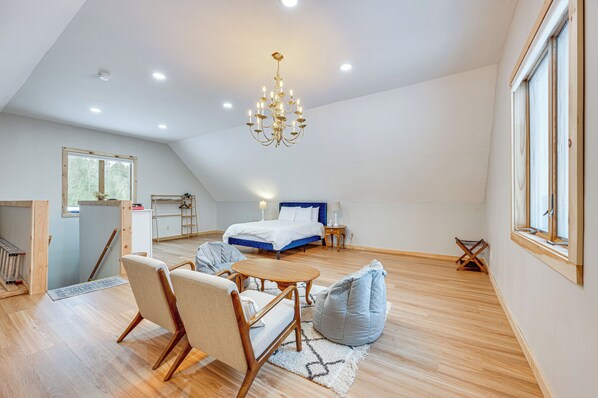 A spacious loft bedroom with a large bed, a chandelier, and a view of the outdoors.