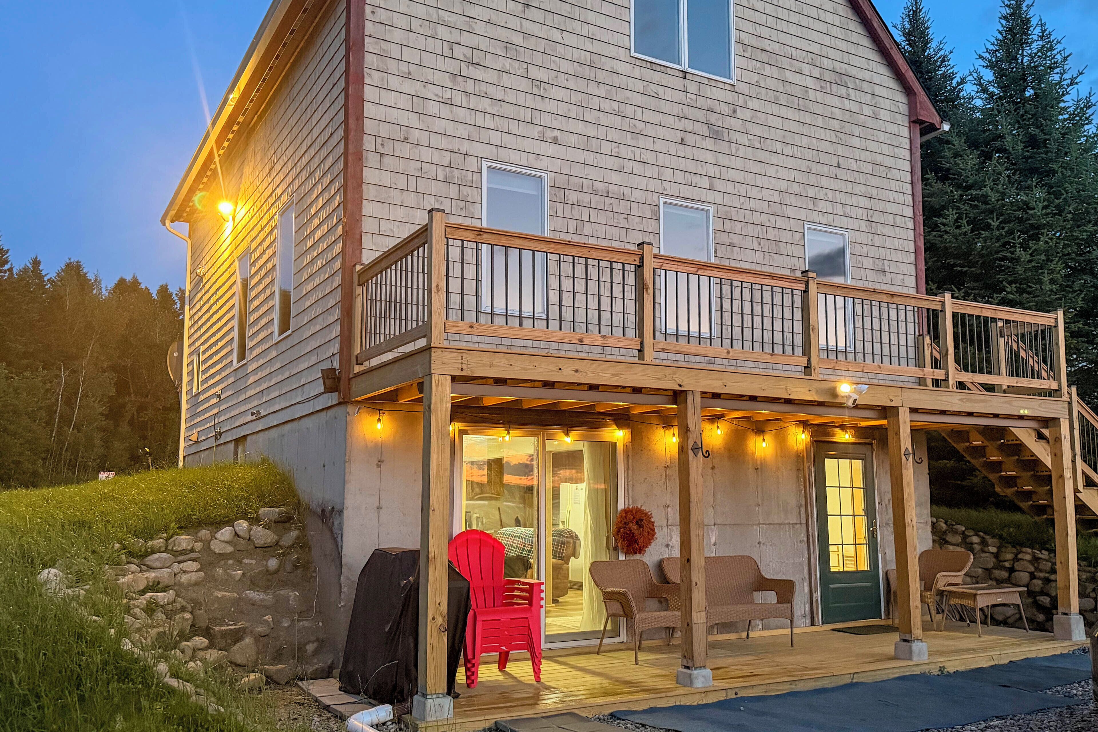 A two-story wooden house with a covered porch, outdoor seating, and a stone wall.