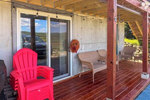 A covered porch with a red plastic chair, a wicker sofa, and a concrete wall. - Cozy Snowmobile Trail Getaway Norton, Vermont (Norton)