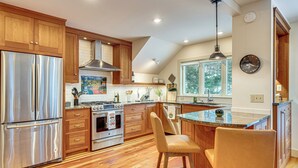 A modern kitchen with wooden cabinets, stainless steel appliances, and a large island with bar stools. - Gorgeous Fall Foliage, Adjacent to Woodstock (Strafford)