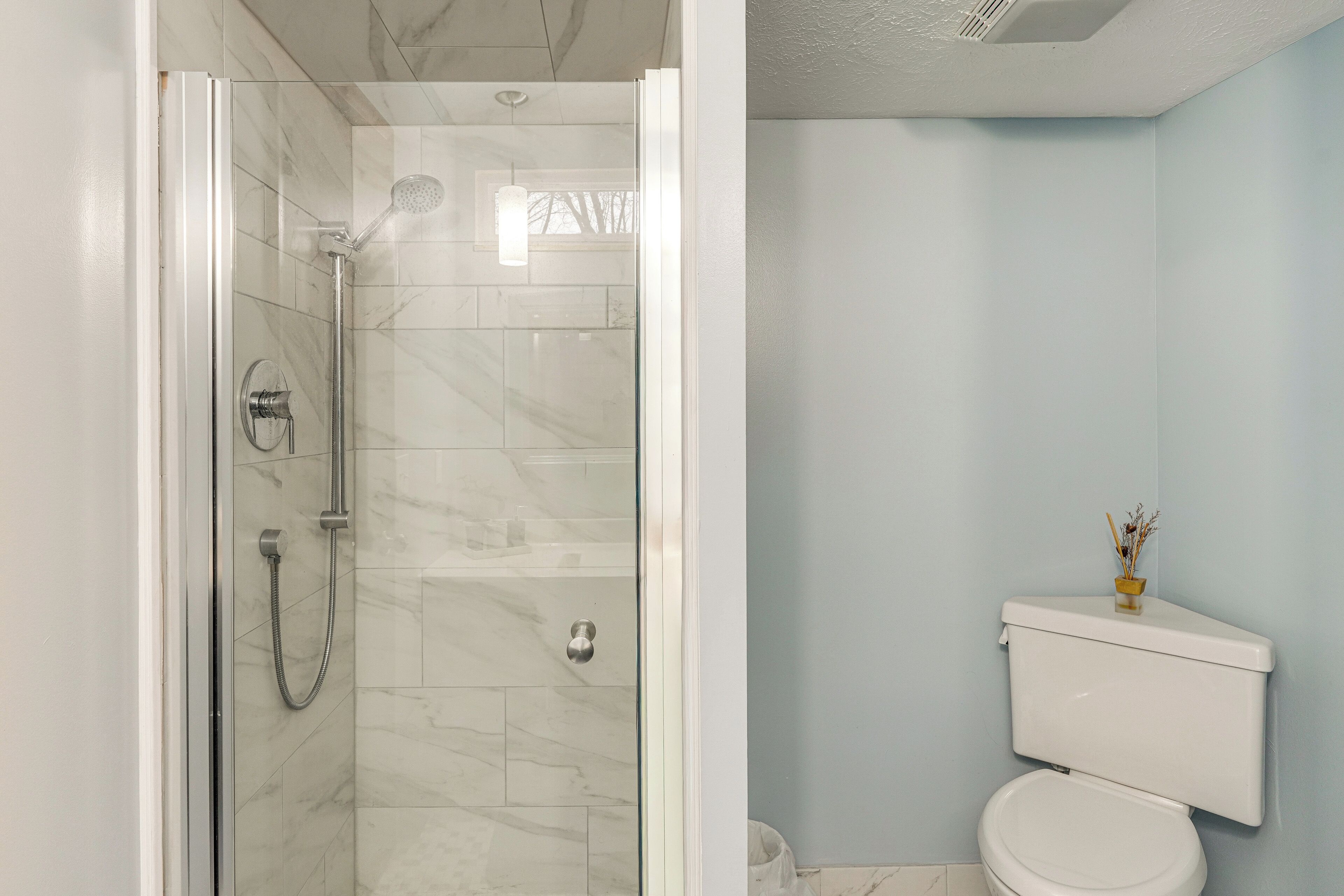 A bathroom with a glass-enclosed shower, a toilet, and a small vase on the toilet tank.