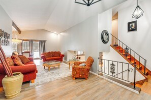 A spacious living room with a red sofa, a patterned armchair, and a glass coffee table. A wooden staircase with a metal railing leads to an upper level. - Close to Hospitals & Downtown: Cleveland Home (North Olmsted)