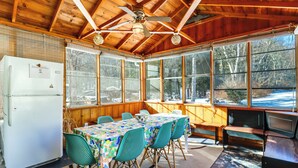 A wooden cabin with a dining area featuring a table and chairs, a refrigerator, and large windows offering a view of the outdoors. - Year-round Fun on Lake Sheridan! Home w/ Patio (Nicholson)