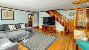 A living room with a grey sectional sofa, a wooden entertainment center, and a staircase with a wooden railing. - Year-round Fun on Lake Sheridan! Home w/ Patio (Nicholson)