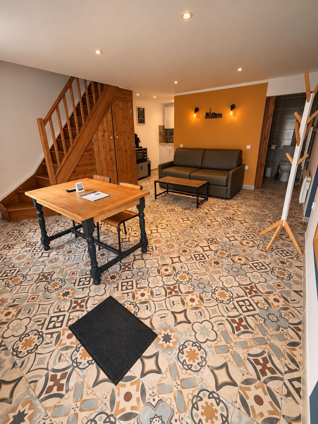 A room with a wooden staircase, a sofa, a coffee table, and patterned floor tiles.