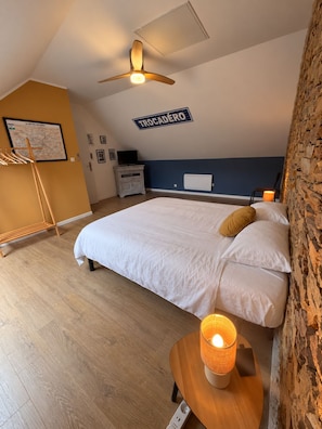 Un dormitorio con cama, ventilador de techo, mapa en la pared, televisor y pared de piedra.
