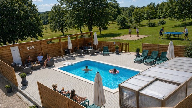 Ett poolområde med solstolar, en bar och en möblerad sittplats under tak.