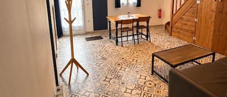 Une pièce avec un sol à motifs, une table à manger avec des chaises, un porte-manteau, un escalier et un téléviseur fixé au mur.