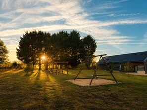 Un parque con un columpio, mesas de picnic y un edificio al fondo.
