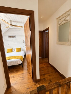 A bedroom with a bed, wooden flooring, a ceiling fan, and a window with a view.