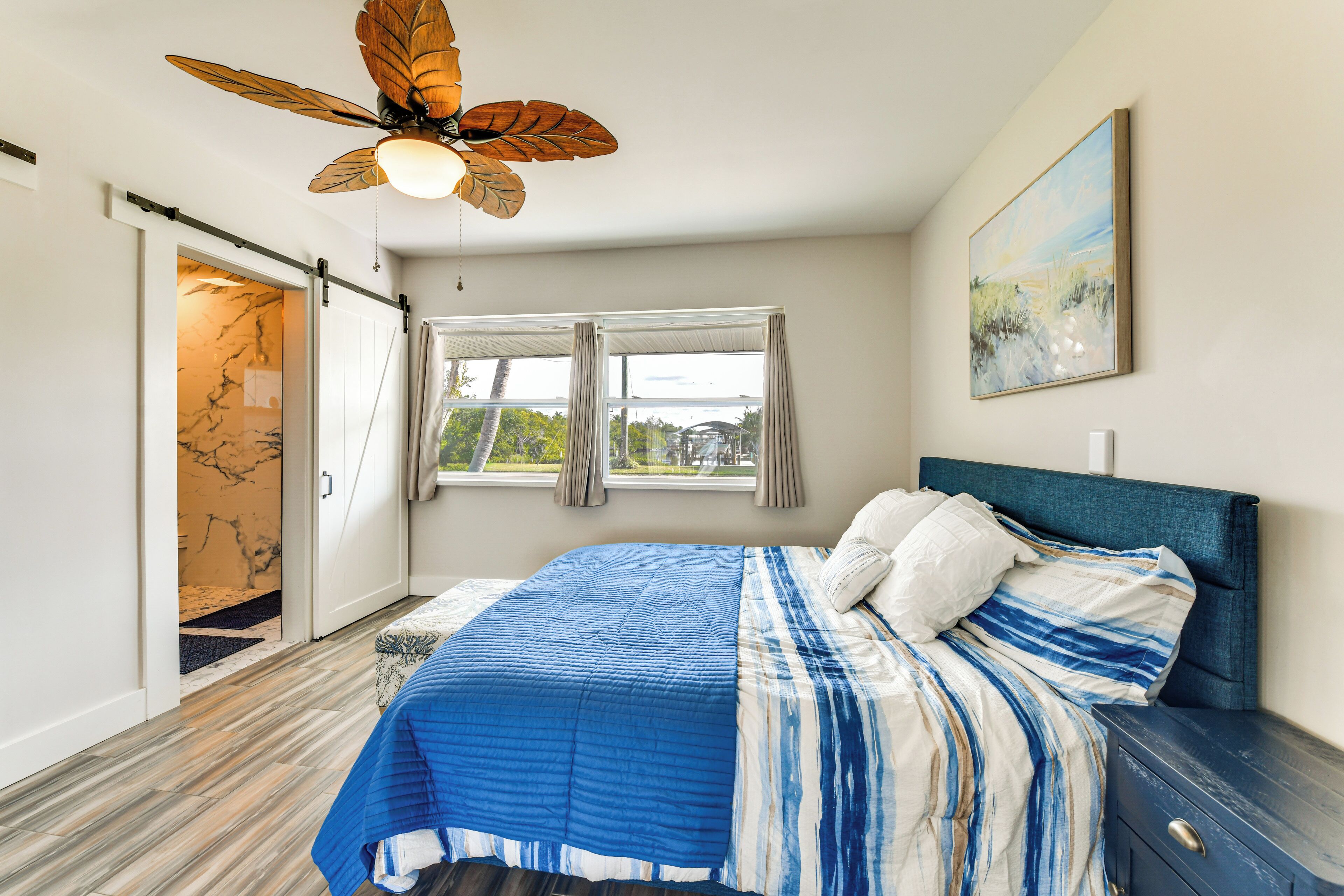 A bedroom with a bed, a ceiling fan, a window with curtains, and a door leading to another room.