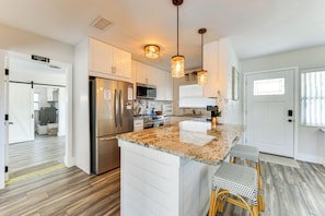 A modern kitchen with white cabinets, stainless steel appliances, a granite countertop, and a dining area with wicker chairs. - Snead Island Getaway! Steps to Bay & Emerson Point (Palmetto)