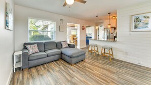 A modern living room with a sectional sofa, wooden flooring, a ceiling fan, and a kitchen area in the background. - Snead Island Getaway! Steps to Bay & Emerson Point (Palmetto)