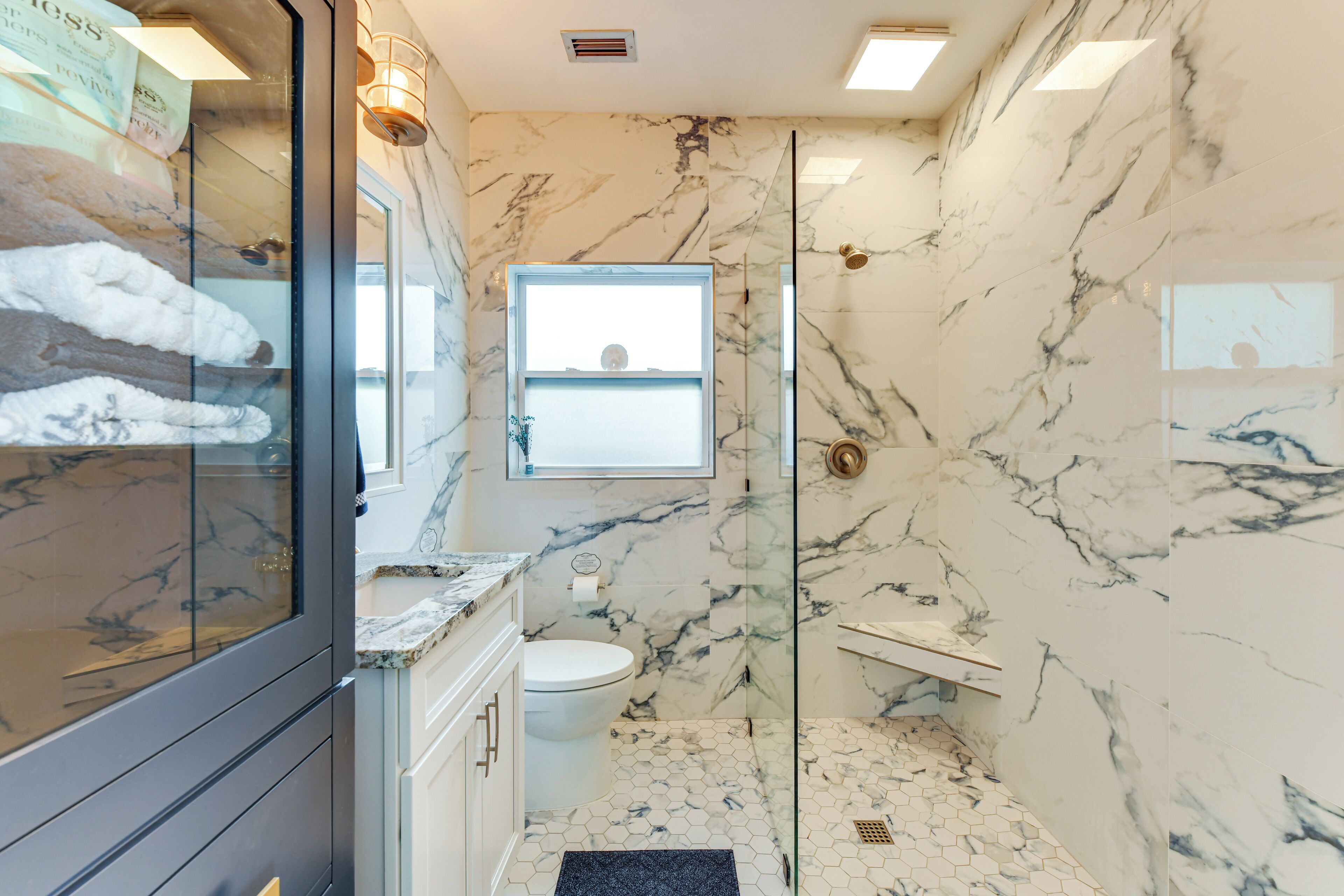 A bathroom with a glass shower enclosure, a toilet, and a vanity with a marble countertop.