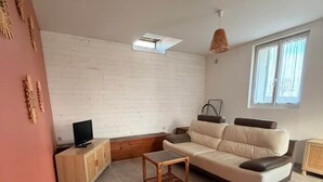 Ein Wohnzimmer mit einer Couch, einem Fernseher, einem kleinen Tisch und einem Fenster.