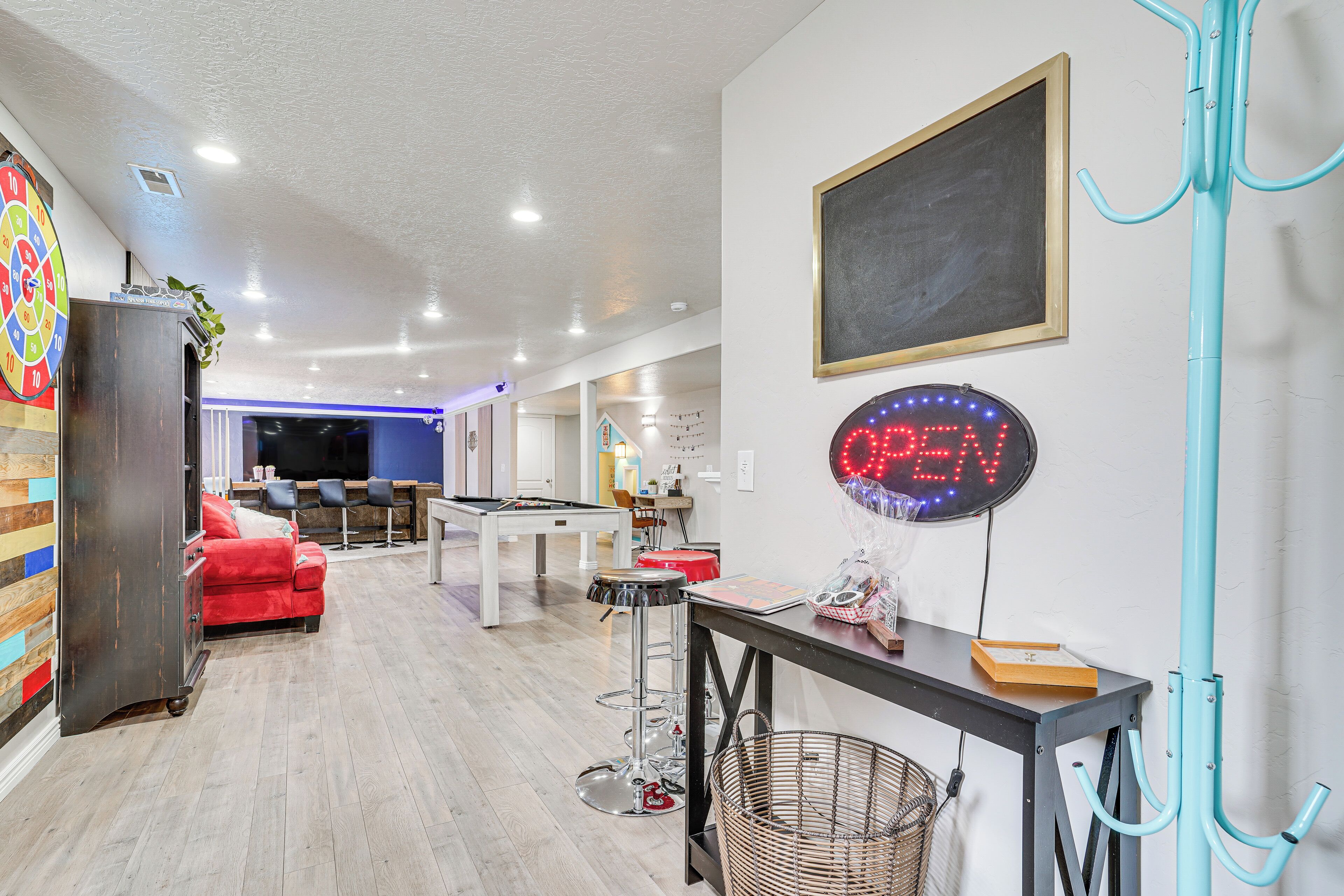 A modern interior with a pool table, red sofa, and a neon 'OPEN' sign.