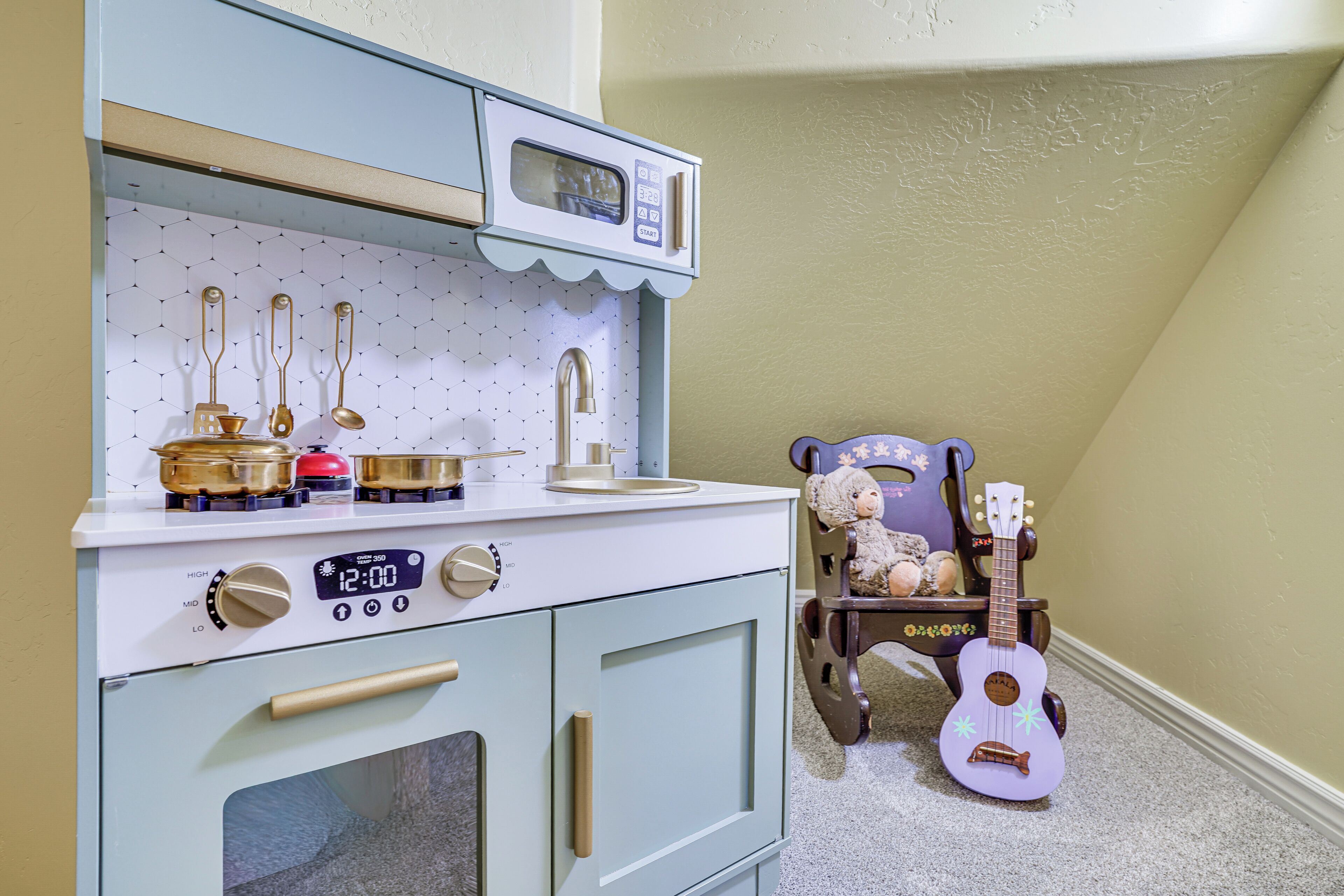 Una cocina equipada con microondas, estufa y diversos utensilios. Se observa un osito de peluche y un ukelele en una esquina.