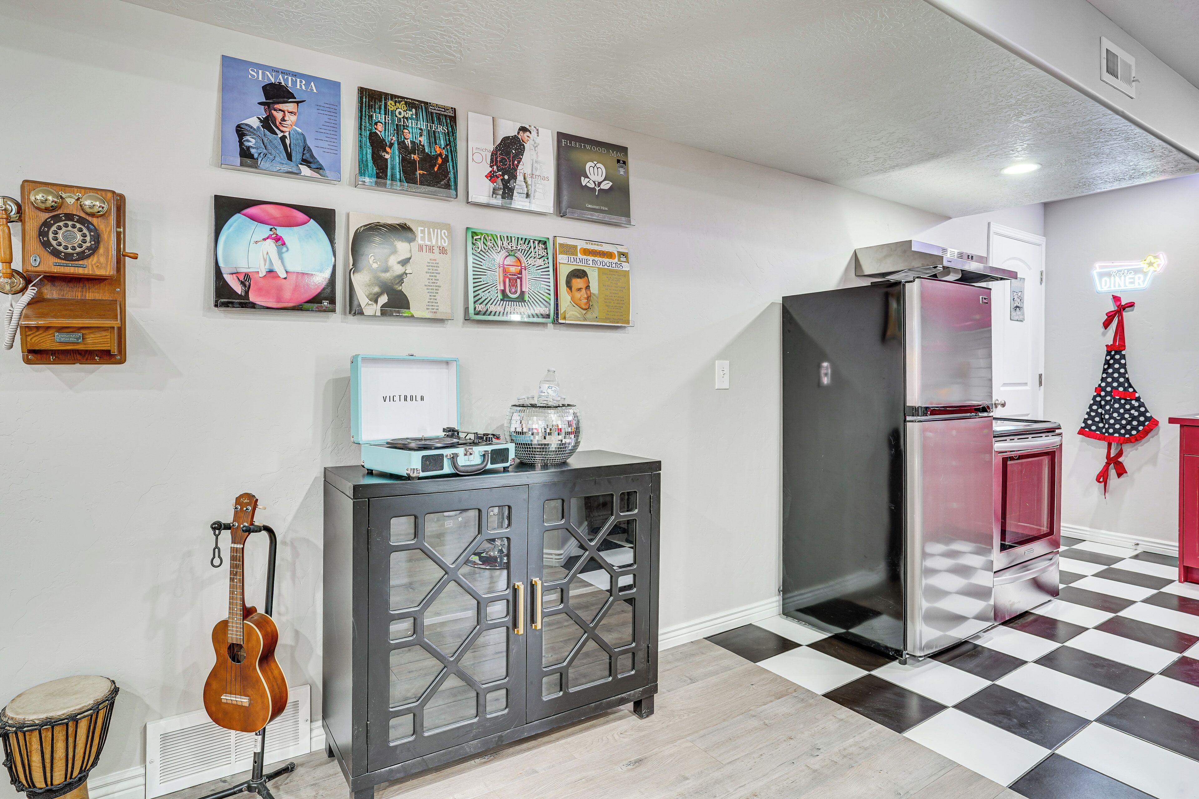 A kitchen with a black and white checkered floor, a refrigerator, a microwave, a cabinet with glass doors, and a wall with framed pictures.