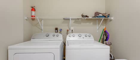Two white Whirlpool front-loading washing machines in a laundry room with a shelf above holding a fire extinguisher and a small stuffed animal.