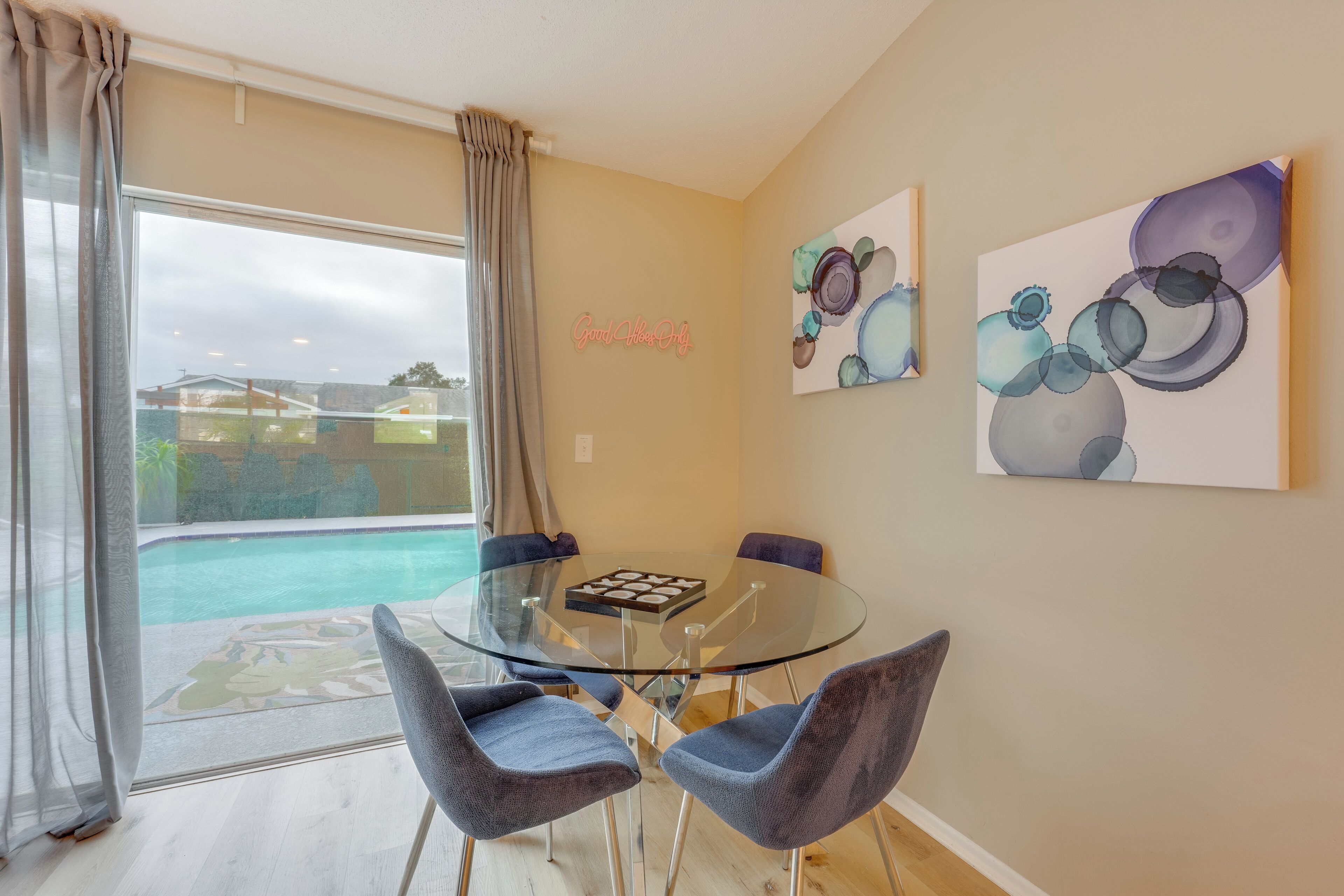 Ein modernes Wohnzimmer mit einem Glastisch, vier Stühlen, Blick auf einen Pool und abstrakter Wandkunst.