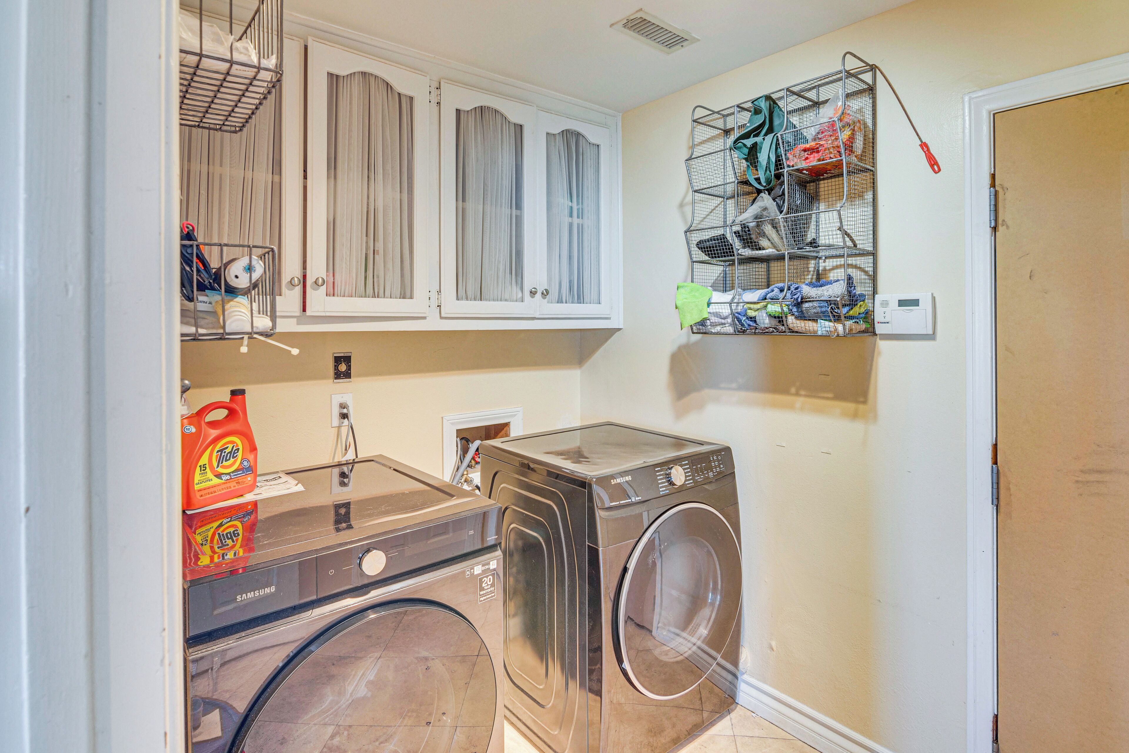 A compact laundry room with a front-loading washer and dryer, a metal drying rack, and a small shelf with cleaning supplies.