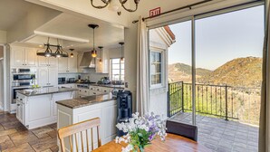 Eine geräumige Küche mit einer großen Kochinsel, ein Essbereich mit Holztisch und ein Balkon mit Blick auf die Hügel.