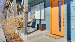 Una casa con una puerta de color naranja brillante, una silla colgante en el exterior y un cielo despejado.