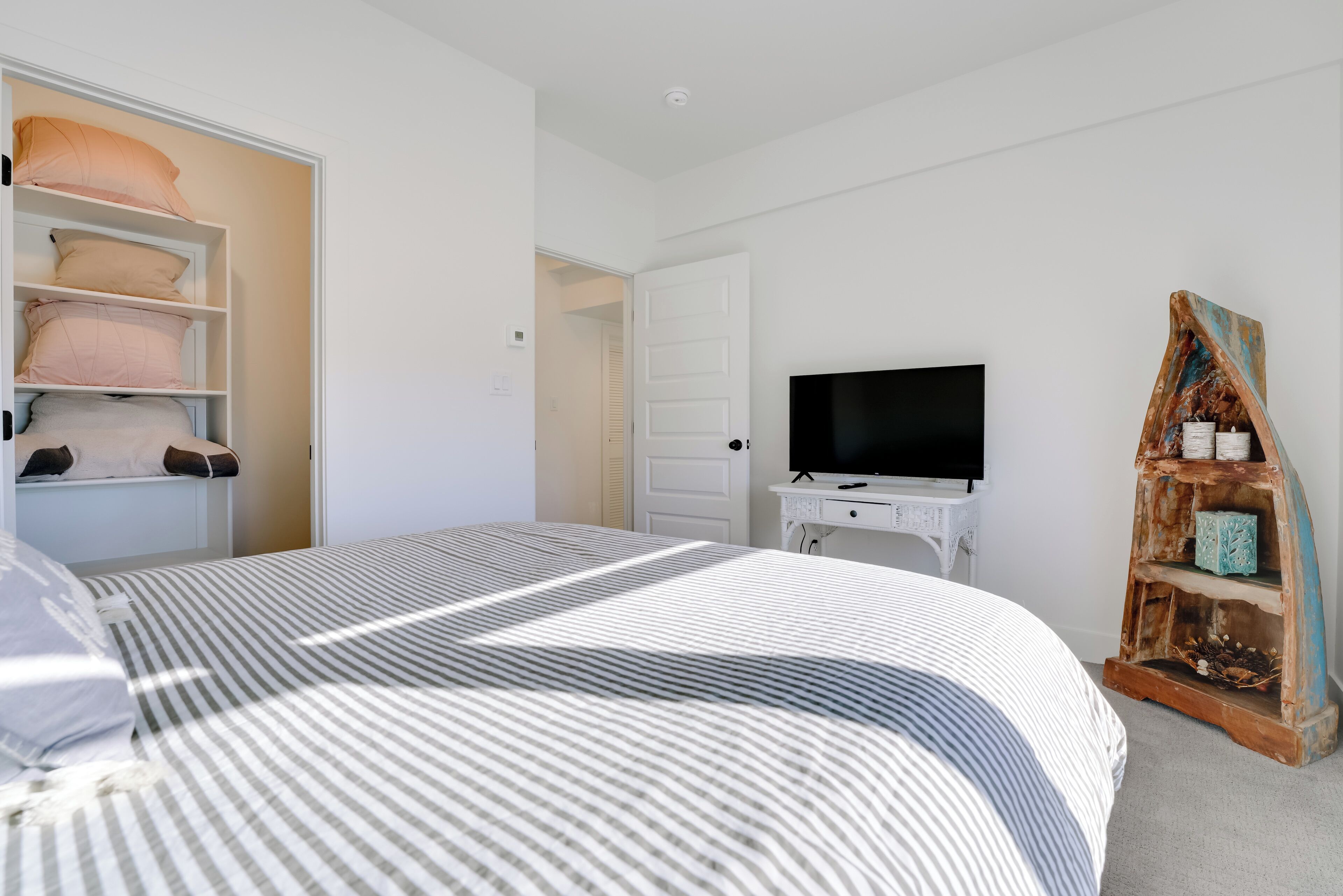 Een slaapkamer met een bed, een televisie, een witte dressoir en een plank met decoratieve objecten.