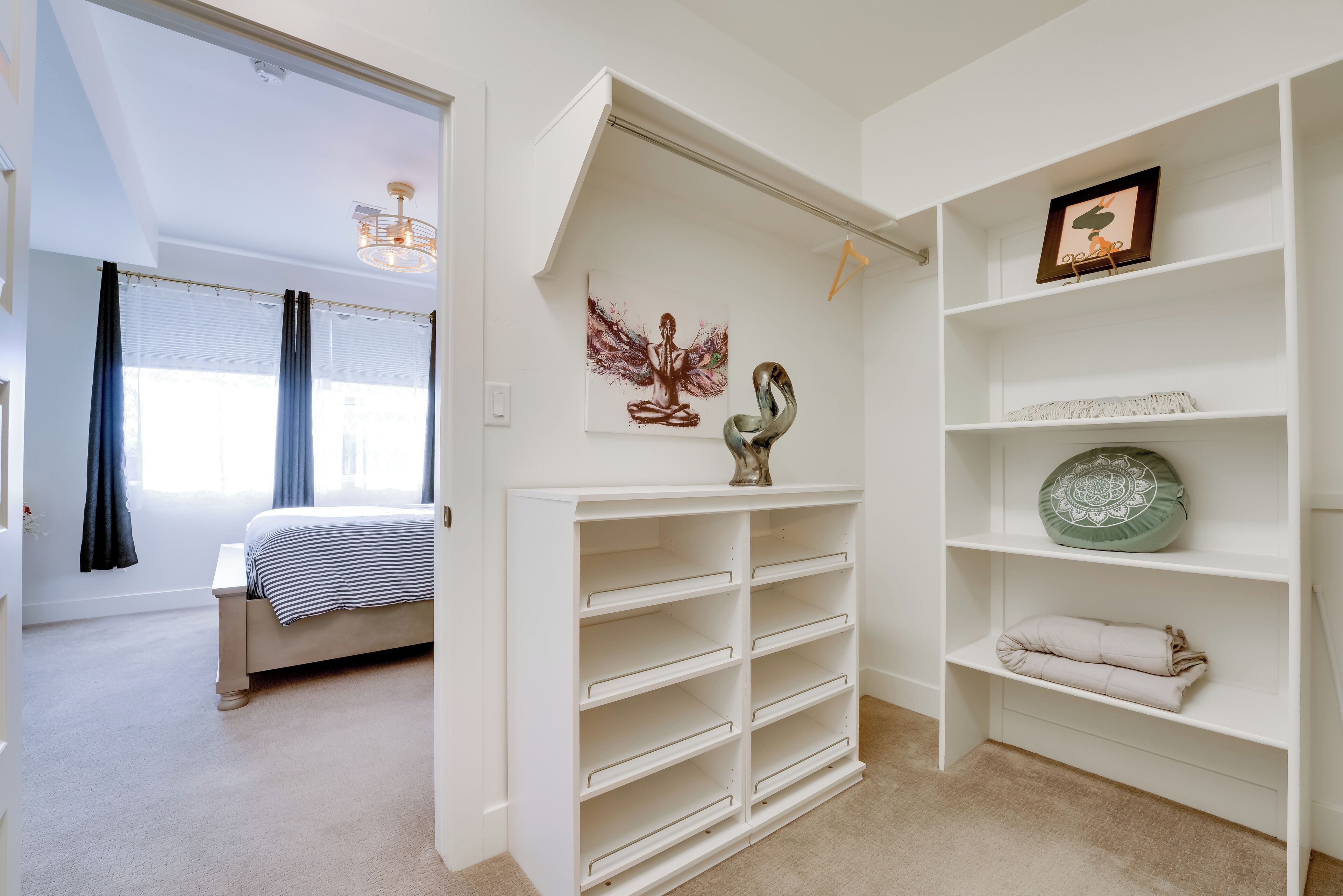A bedroom with a bed, a white shelving unit with decorative items, and a view into another room.