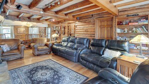 A log cabin interior with leather sofas, a patterned rug, wooden beams, and a bookshelf with various items. - Hike, Fish & Boat Nearby! Bloomington Family Cabin (Bloomington)