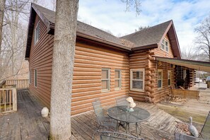 A log cabin with a wooden deck, outdoor seating, and a covered area.