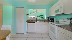 A kitchen with white cabinets, a microwave, and a sink. There is a window with plants and a hanging light fixture.