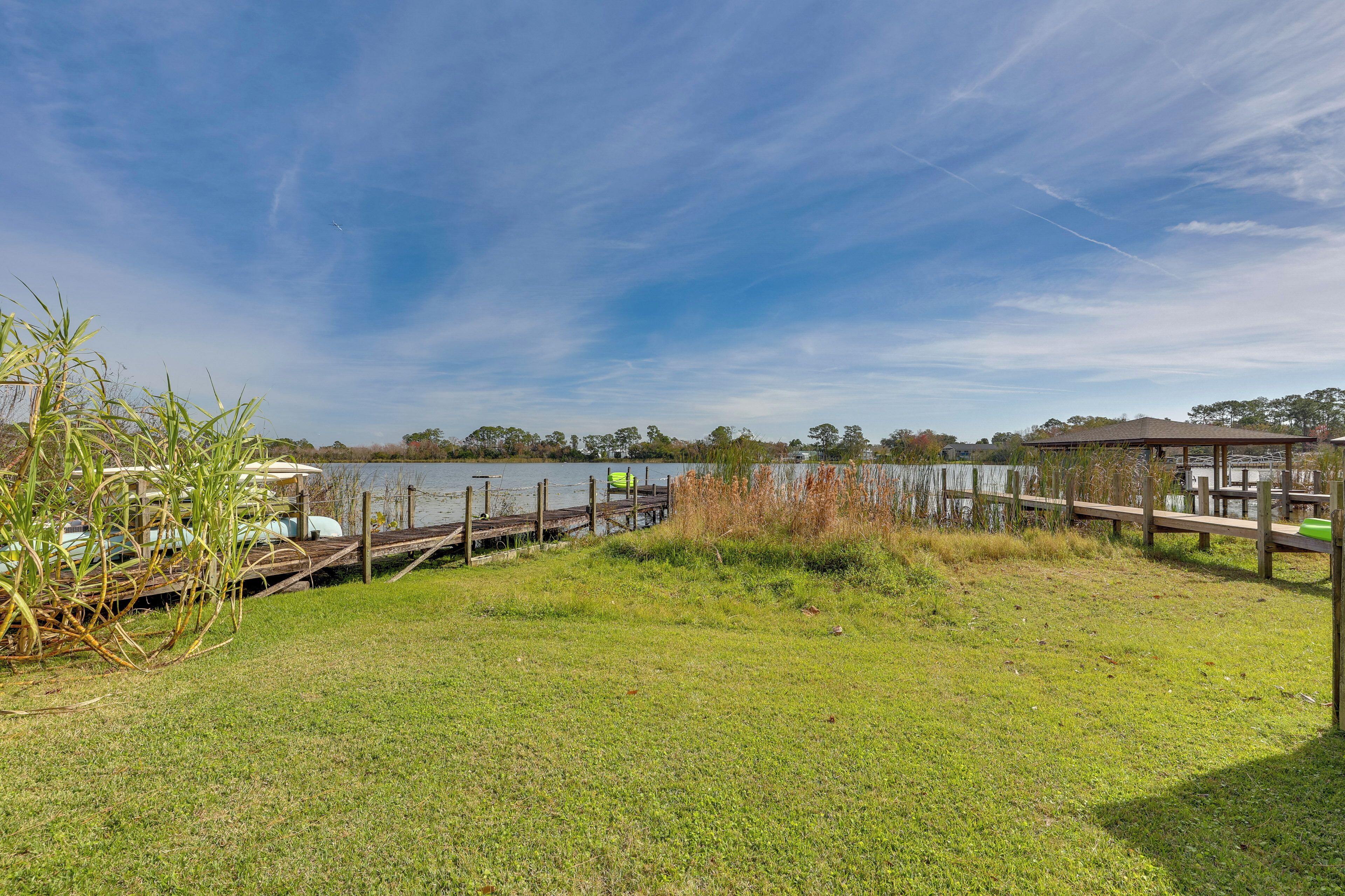 Un parque junto al lago con un muelle de madera, zonas verdes y un pabellón.