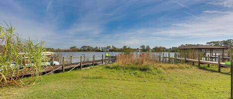Un parque junto al lago con un muelle de madera, zonas verdes y un pabellón.