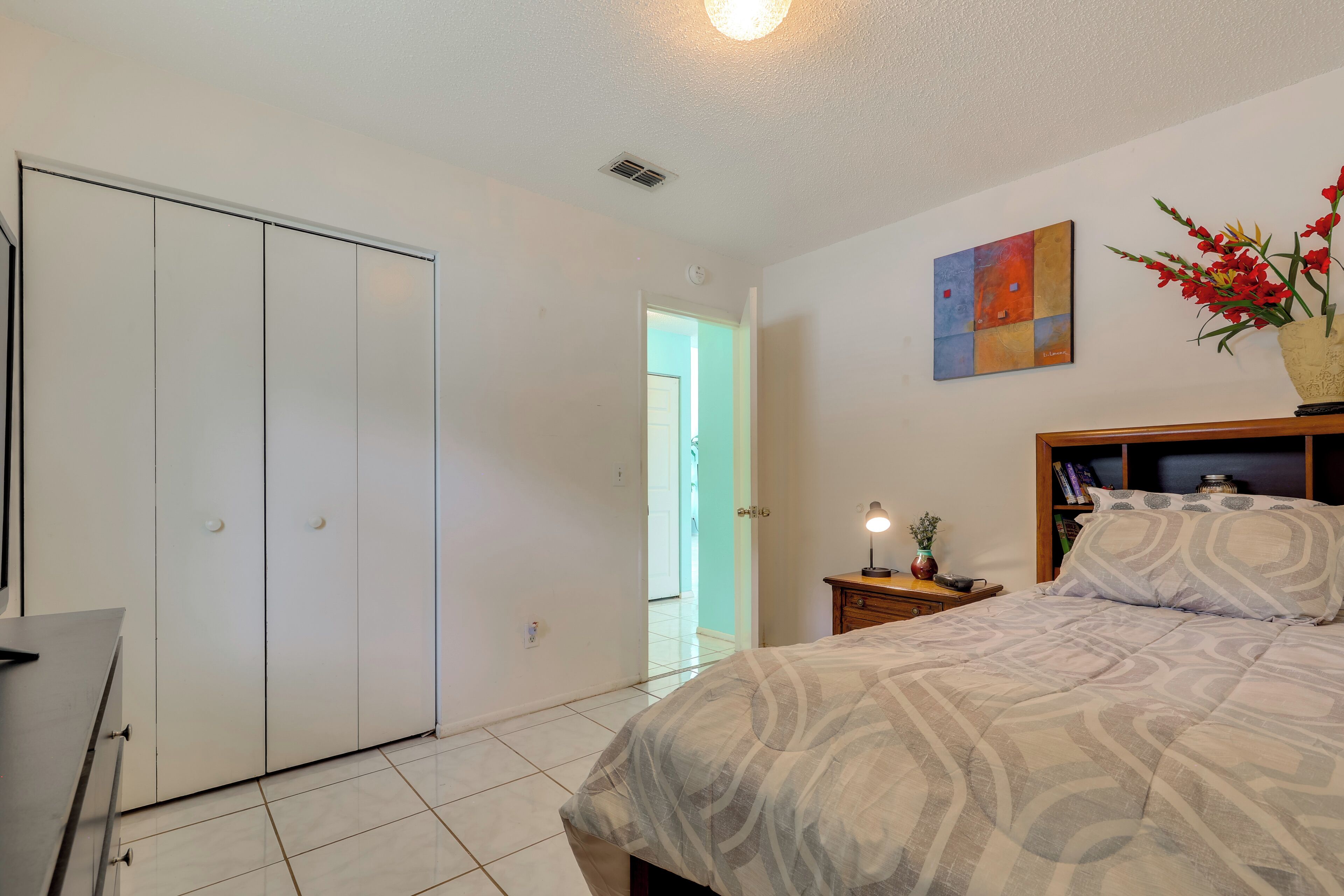 Une chambre à coucher avec un lit, une table de chevet, une lampe, un vase avec des fleurs et une armoire.
